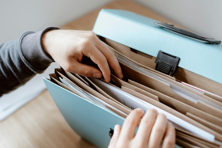 Hands in gray sweater organizing documents in light blue file folder with manila dividers, showing simple document management