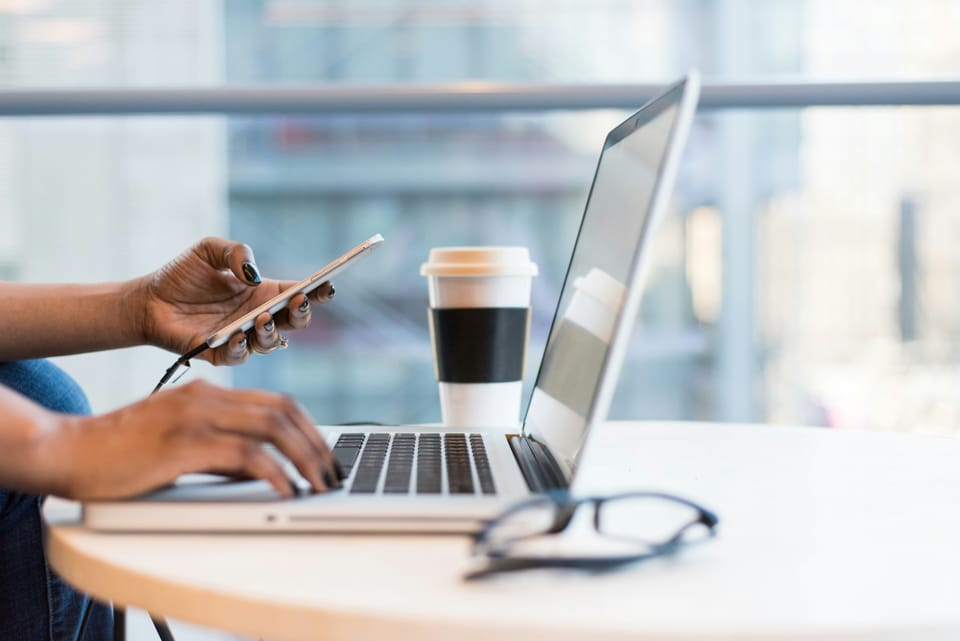 Business owner working on a clean workspace with laptop, glasses, cell phone, and coffee cup on adesk, ready for planning